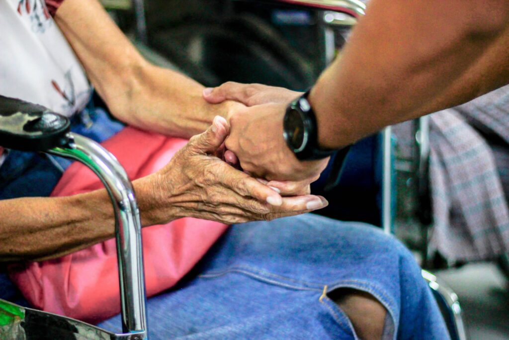 Close up of two people, one youthful and one elderly holding each other hands tenderly