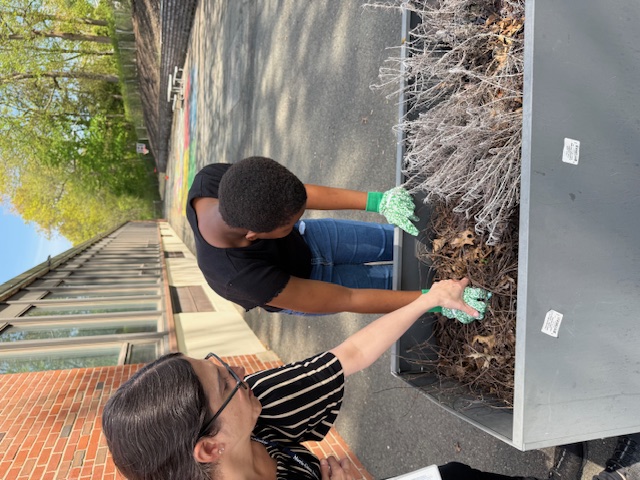 Teacher and student working on a large gray planter outdoors