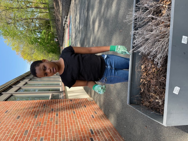 Student standing behind a large gray planter outside of the school