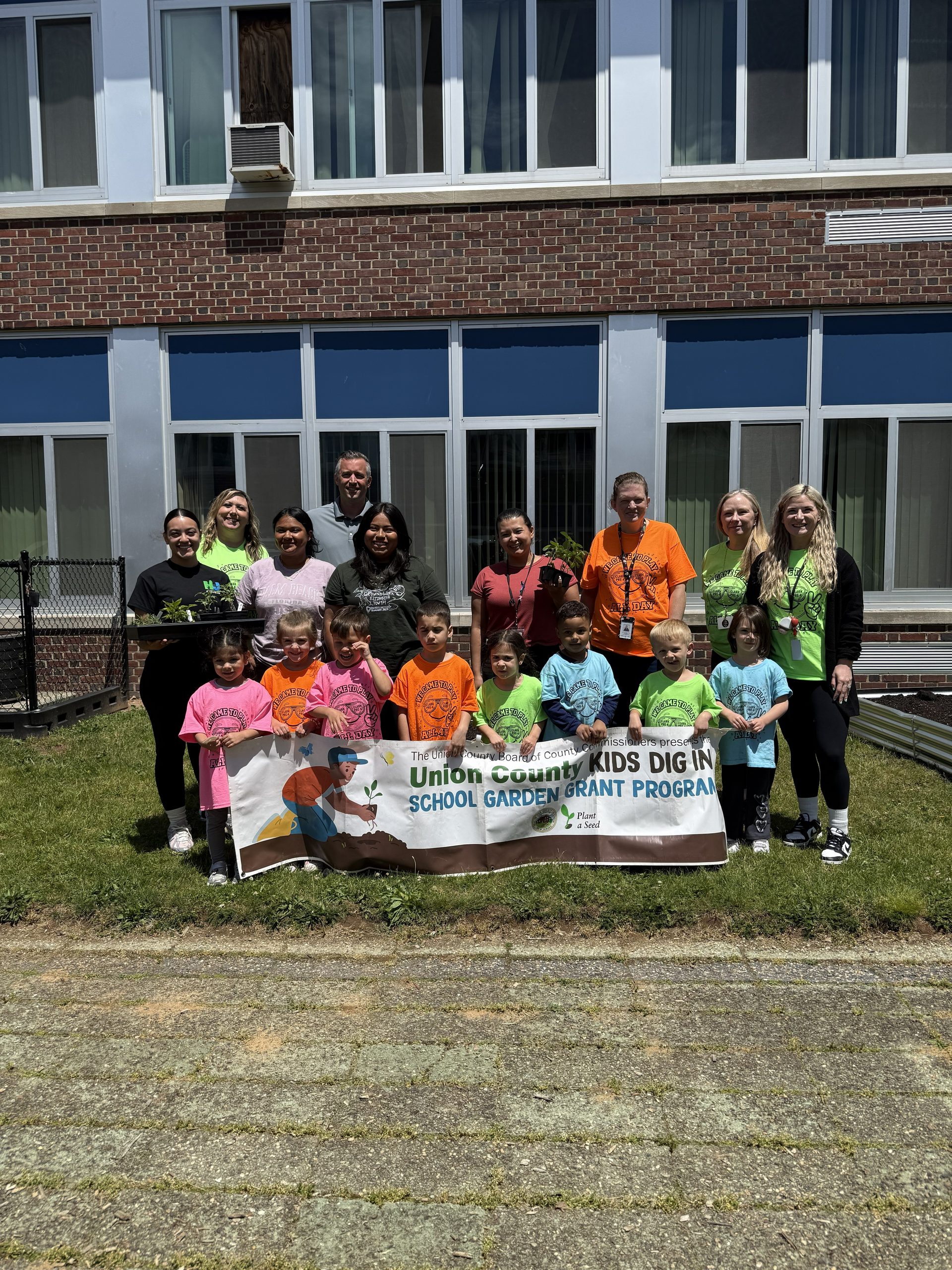 Image of Clark Pre-K students, faculty, and Groundworks Elizabeth staff posing for this picture, while kids proudly hold up their Kids Dig In Garden Grant banner