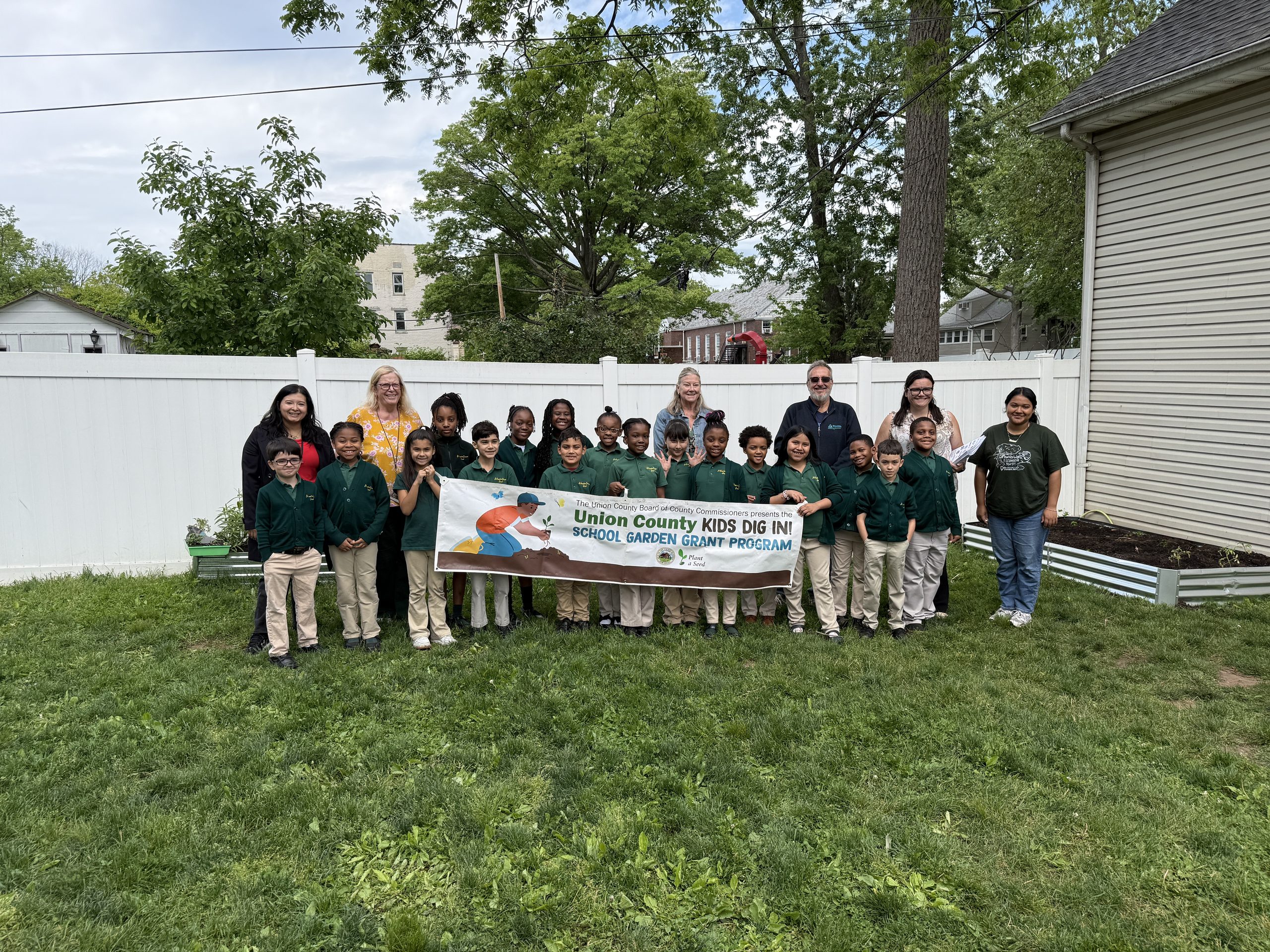 St. Joseph students, teachers, and Groundwork Elizabeth gardeners proudly pose for a picture as they hold up their Union County Kids Dig in School Garden Grant Program sign