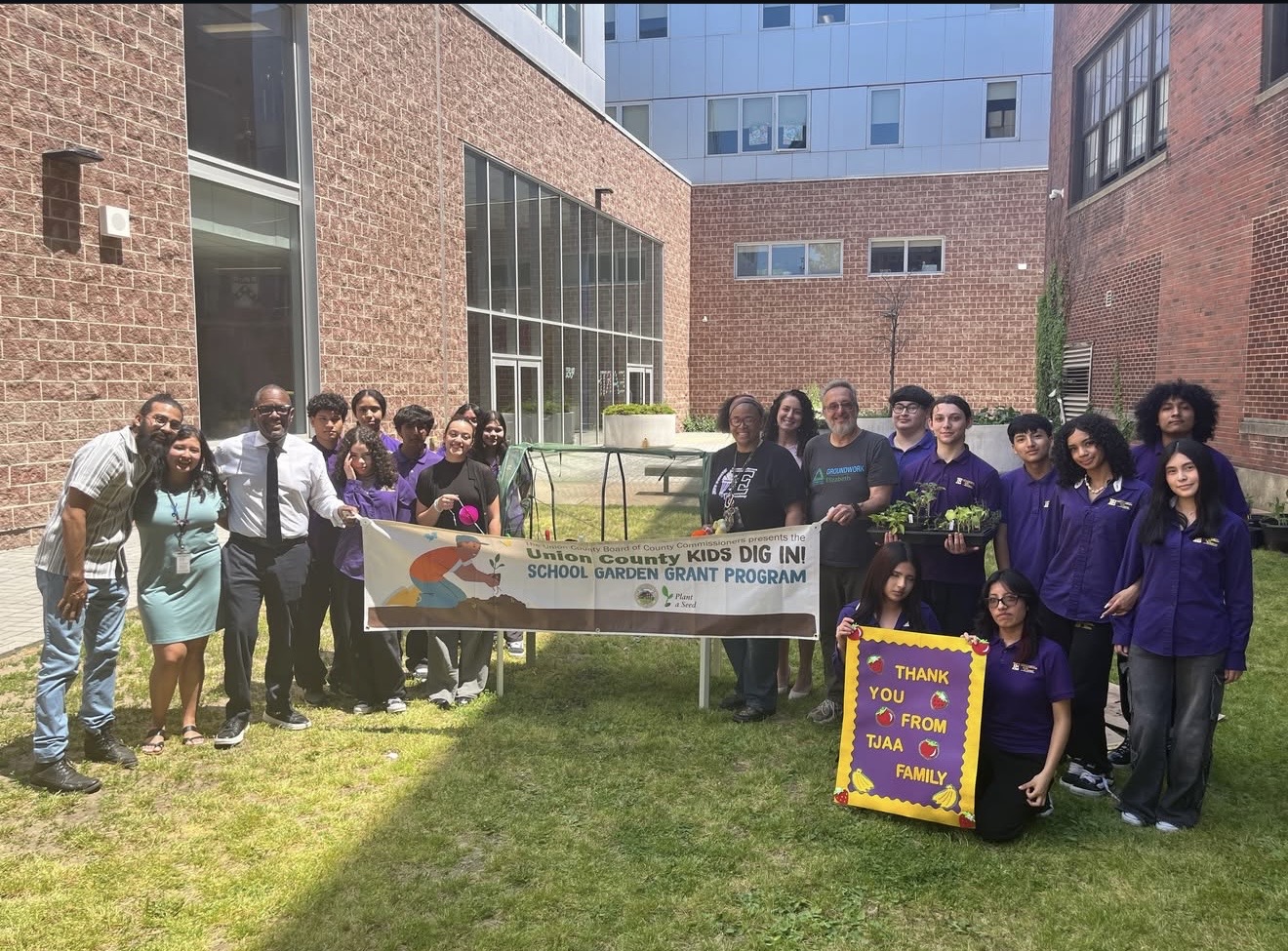 Thomas Jefferson Arts Academy (TJAA) students, staff, Groundworks employees, Union County representatives and Commissioner Stanley Neron pose with Kids Dig In Garden grant banner 