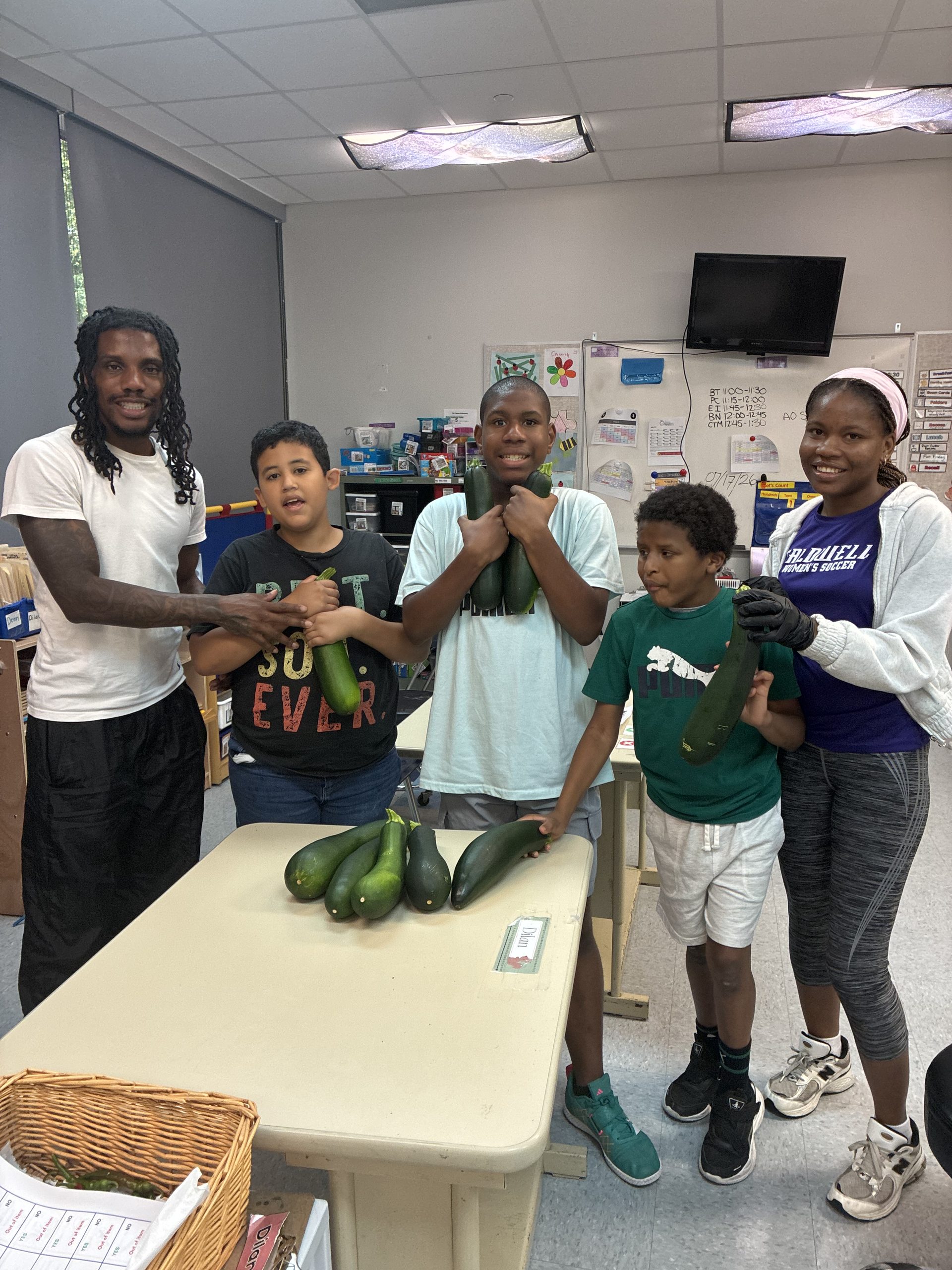 Photo of Crossroads students and adults holding and displaying large healthy zucchinis harvested from the garden