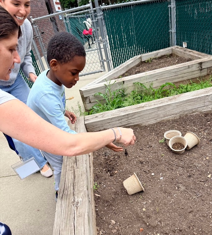 Image of teacher and student planting seeds in the raised garden bed. 
