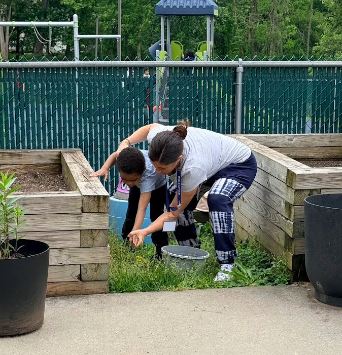image of teacher helping student remove weeds from the ground surrounding the raised garden beds. 
