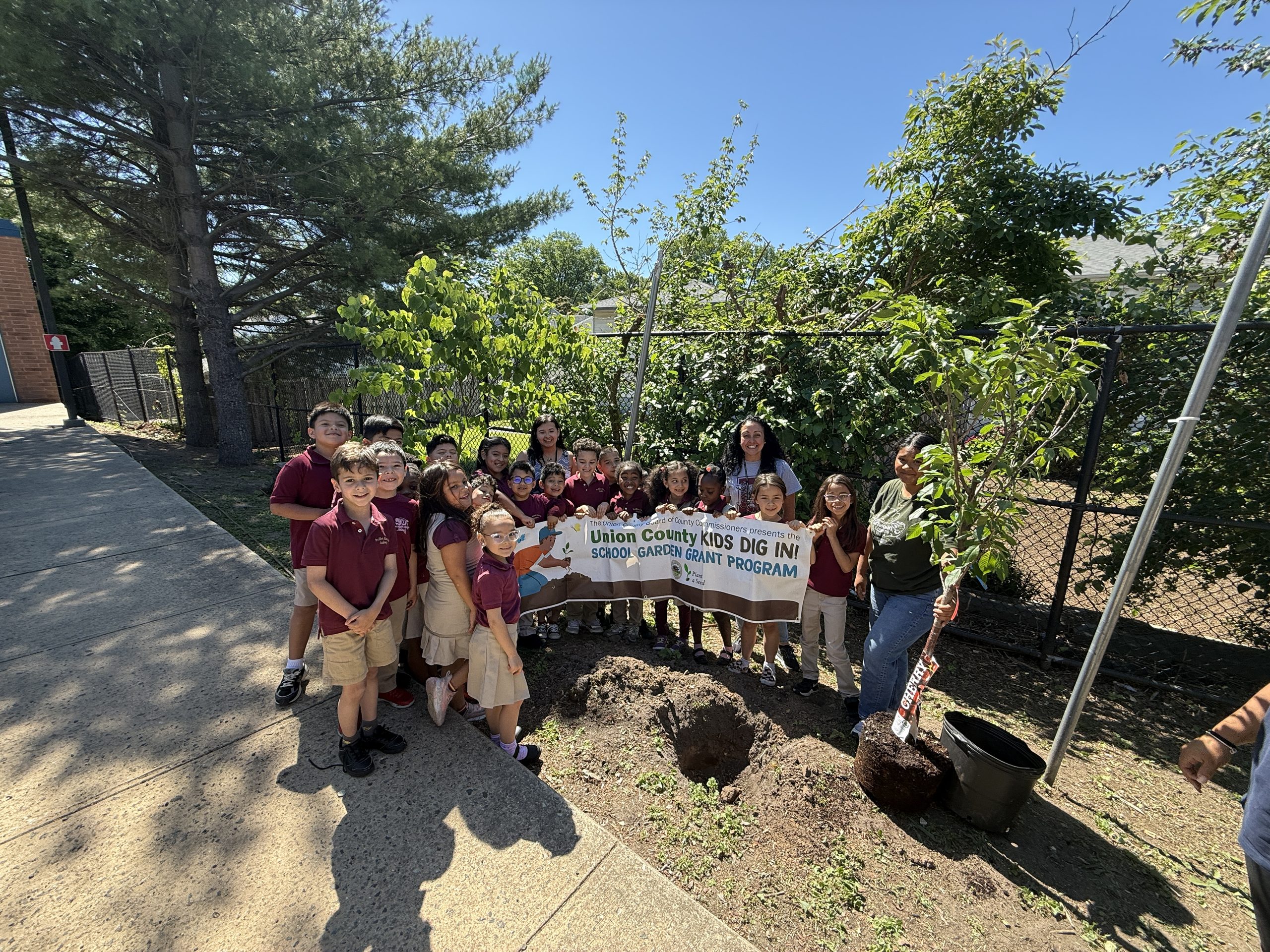 Dr. Albert Einstein Academy students, teachers, and Groundworks Elizabeth representatives smiling while holding up their Kids Dig In School Garden Grant banner