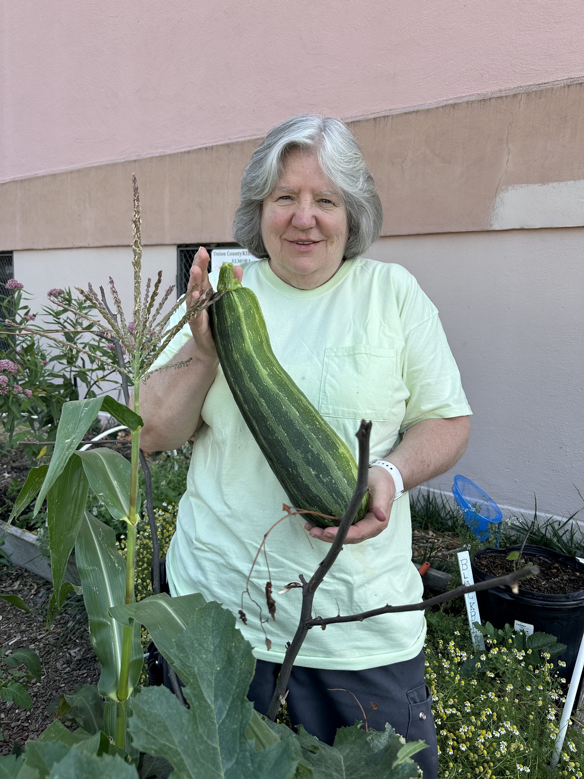Lady in a green t-shirt holding up a green striped zucchini