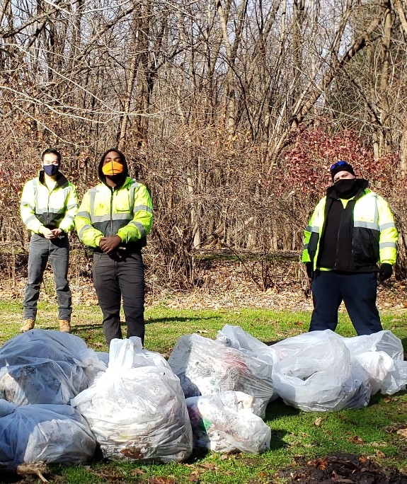 three people proudly standing behind full garbage bags from cleaning up the park