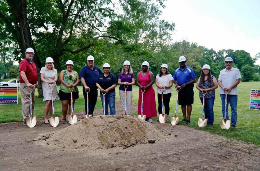 people with hard hats and shovels standing behind broken ground for a photo