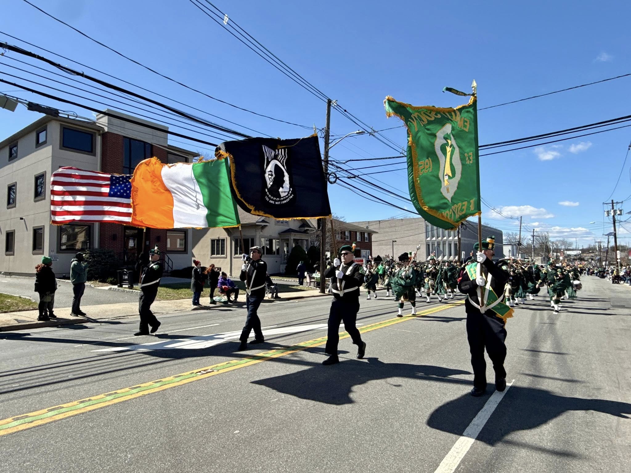 Image of a colorful St. Patrick's Day parade procession featuring flag bearers, marching bands, and decorated floats celebrating Irish culture