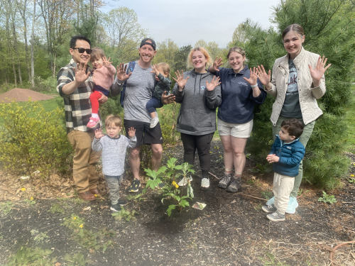 Image of families with young kids on a Toddler Time nature walk/ Families are smiling and displaying hands after getting a plant in the ground